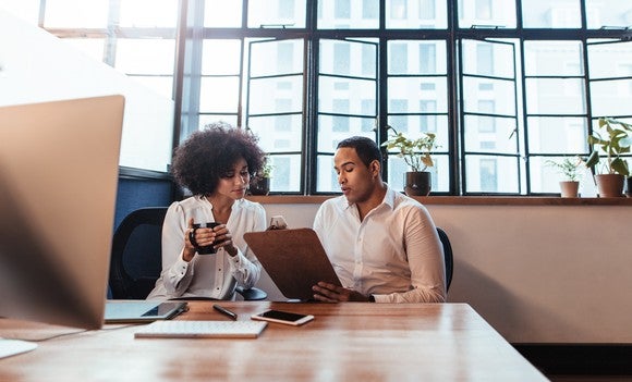 Professional male and female having a discussion while seated at a desk